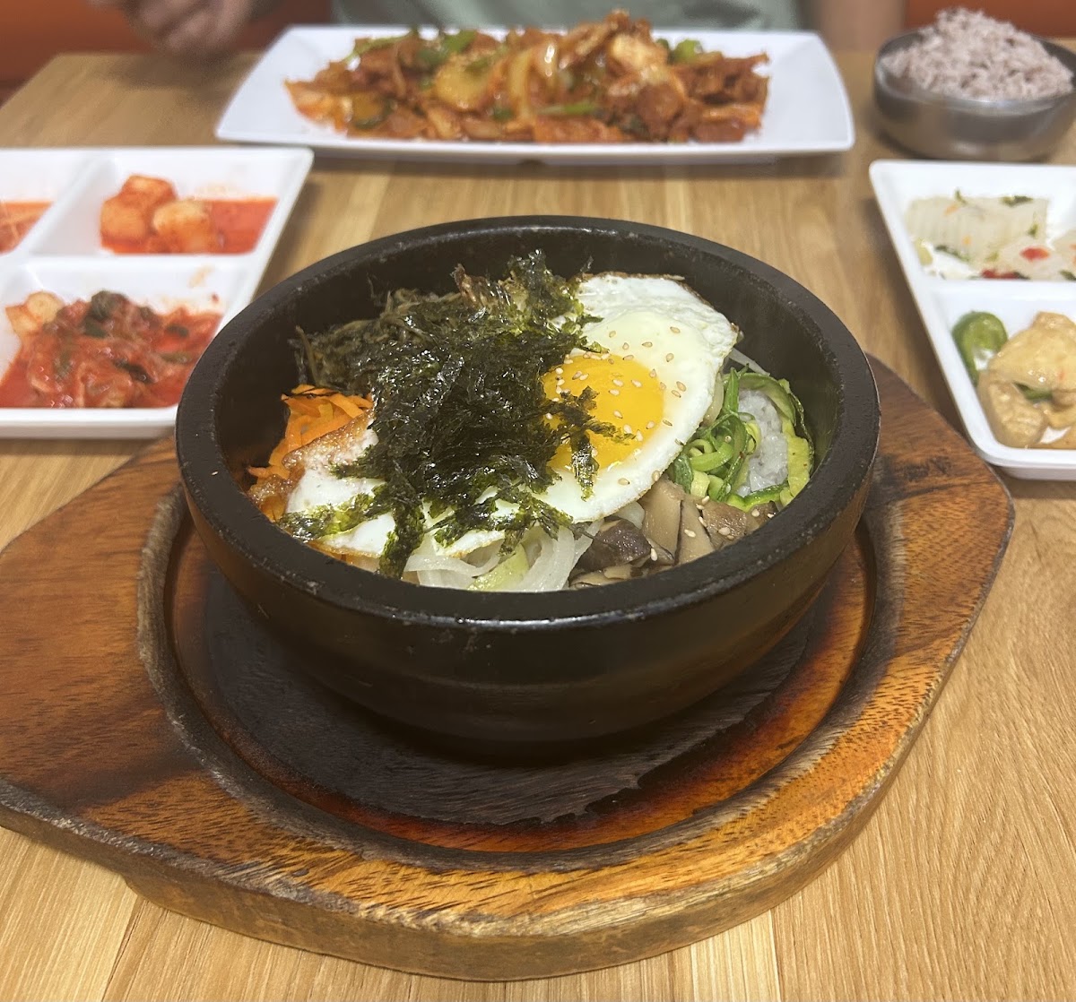 Stone pot bibimbap topped with a fried egg and seaweed, surrounded by side dishes