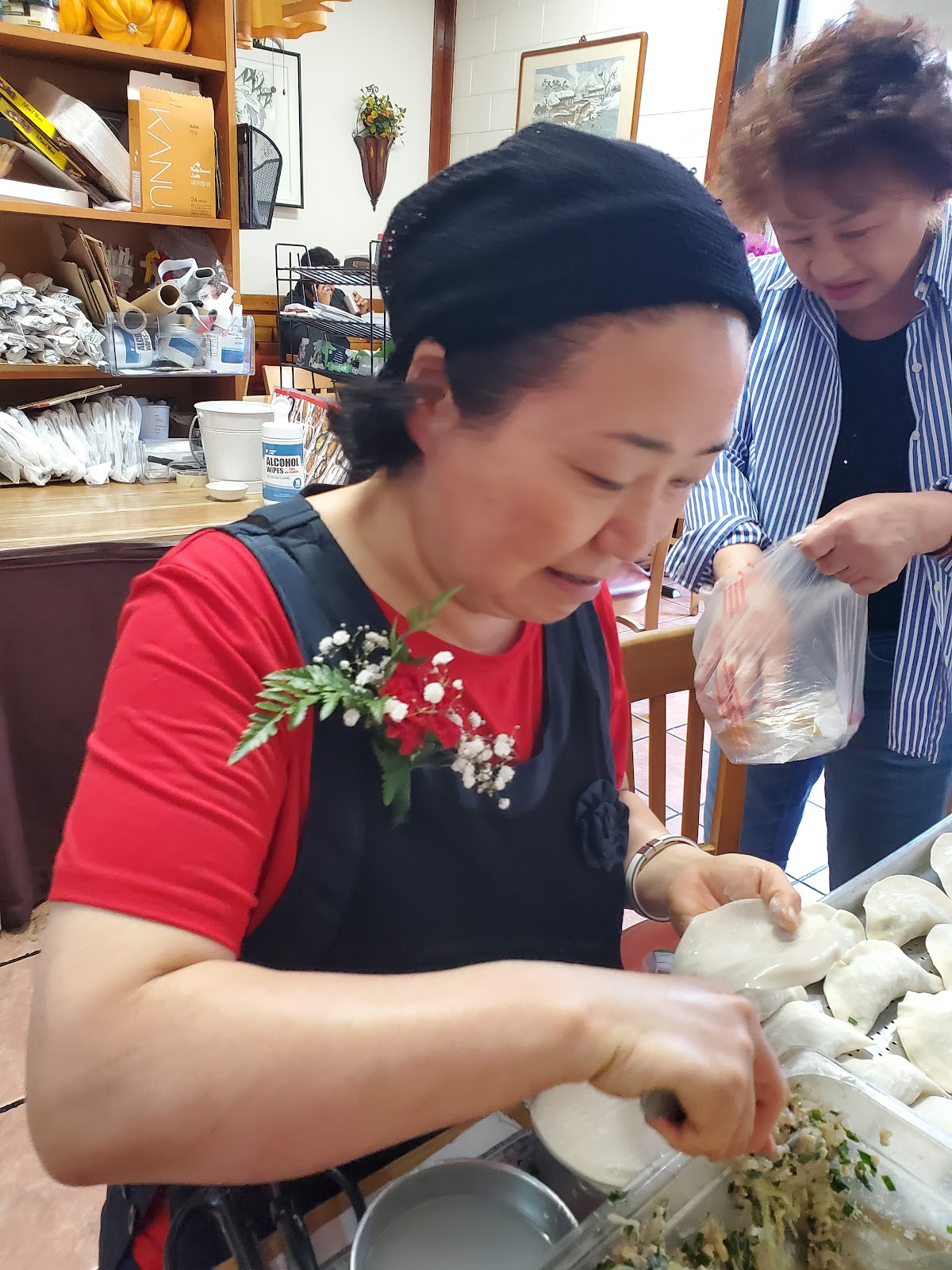 One of the owners folding dumplings by hand at the counter while a second woman bags them